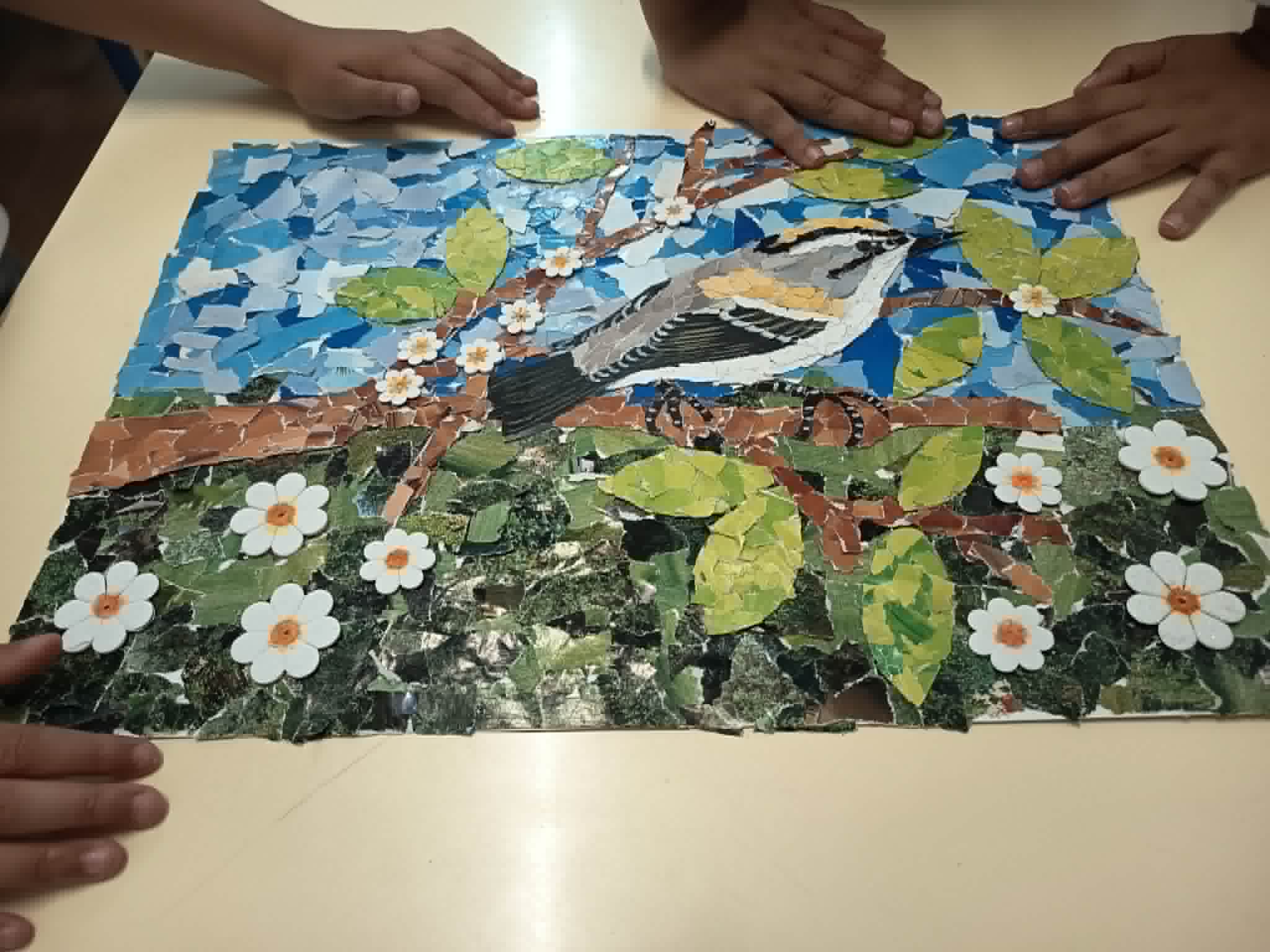 Composição final do trabalho artístico – as mãos dos alunos envolvem a obra, simbolizando a proteção, o cuidado e o compromisso coletivo com a preservação do habitat do bis-bis e da Floresta Laurissilva.
