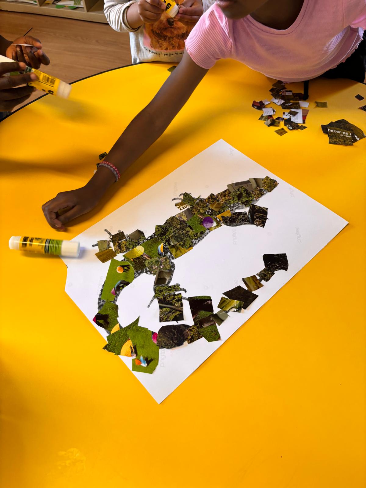 Detalhe do processo de construção da colagem, evidenciando a aplicação dos recortes e o preenchimento da figura do lagarto. As crianças participaram ativamente na escolha e colocação dos materiais.